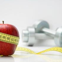 Apfel mit Maßband und Hanteln im Hintergrund
